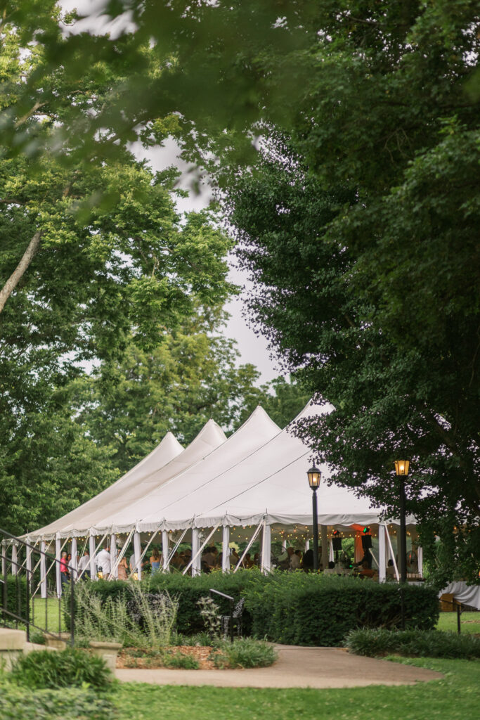 A wide shot of a tent set in the garden at Whitehall. A wedding reception is taking place in the late spring. 
