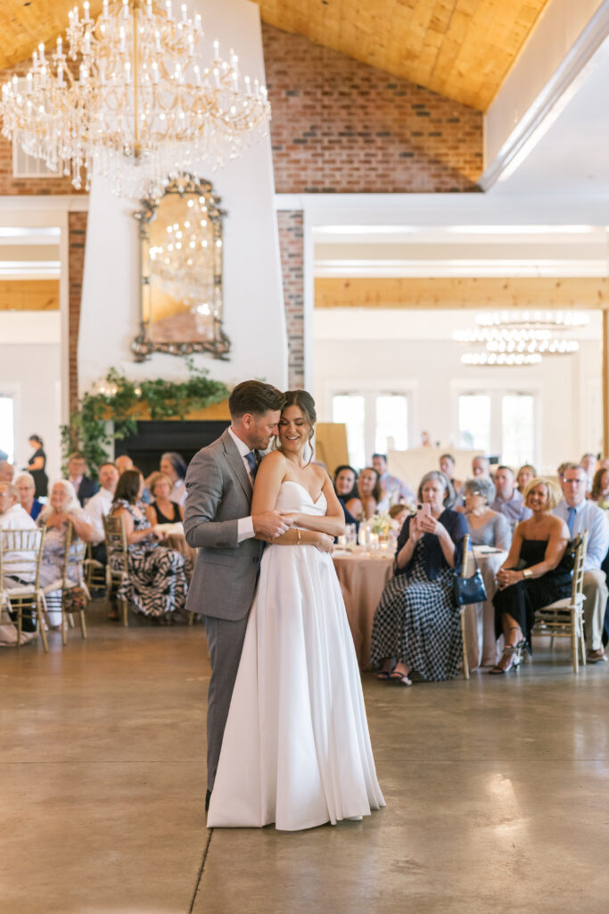 A couple during their first dance at Hazlenut Farms. The couple is wrapped in a warm embrace. Guest are seen in the background admiring the couple. 