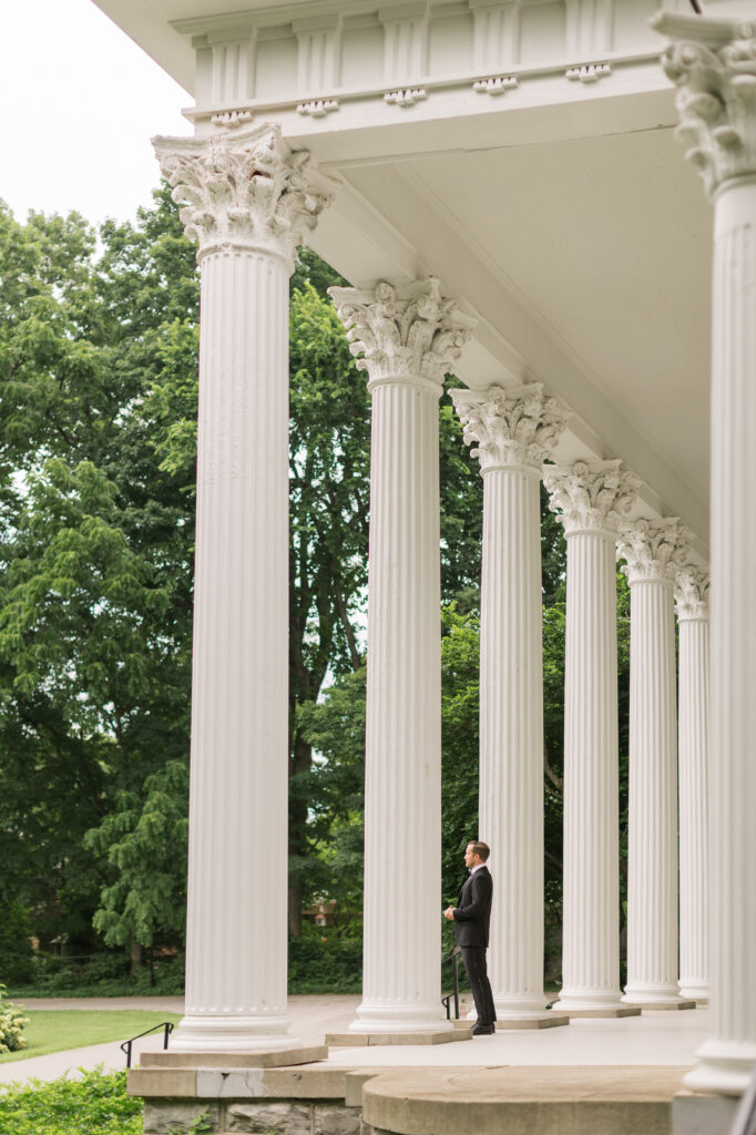 A groom standing on the grand porch at Whitehall looking off into the distance before the ceremony. 